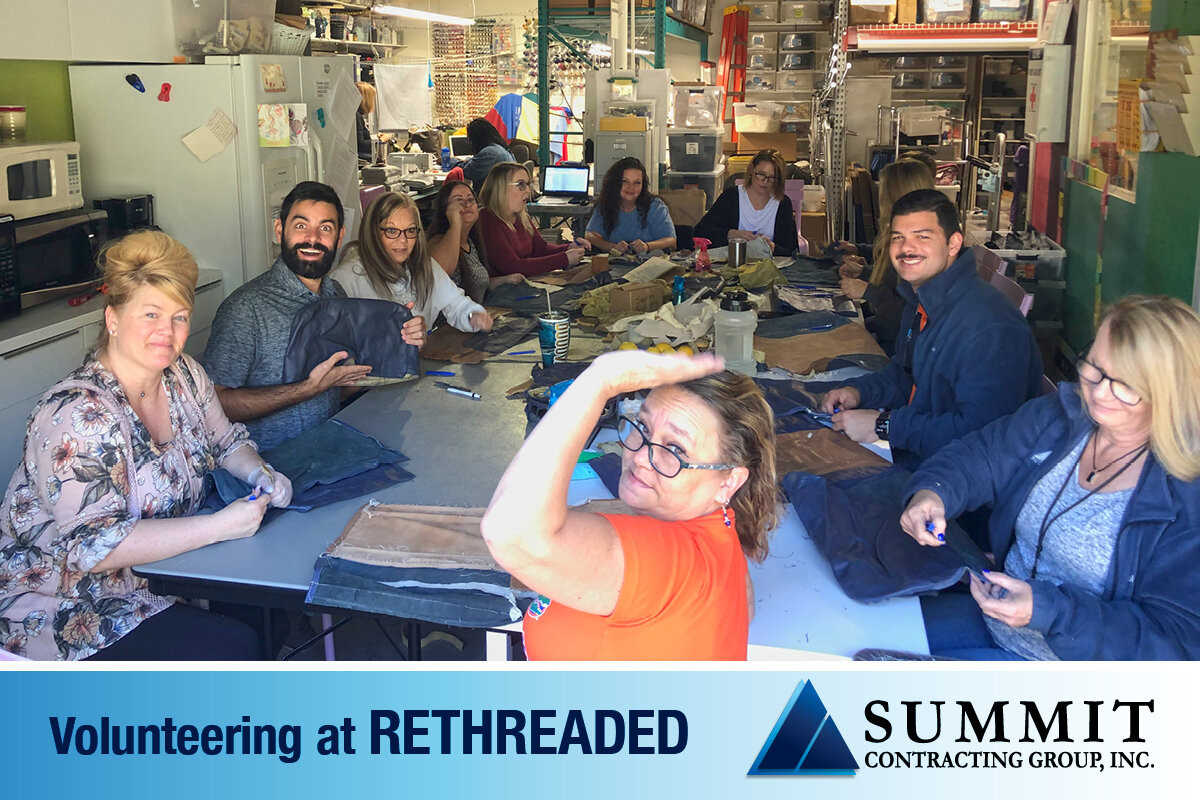 Summit Employees smiling and waving to camera while stitching clothes at a volunteer event