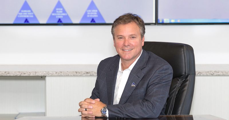 Man in suit with Summit pin sitting at desk and smiling to camera