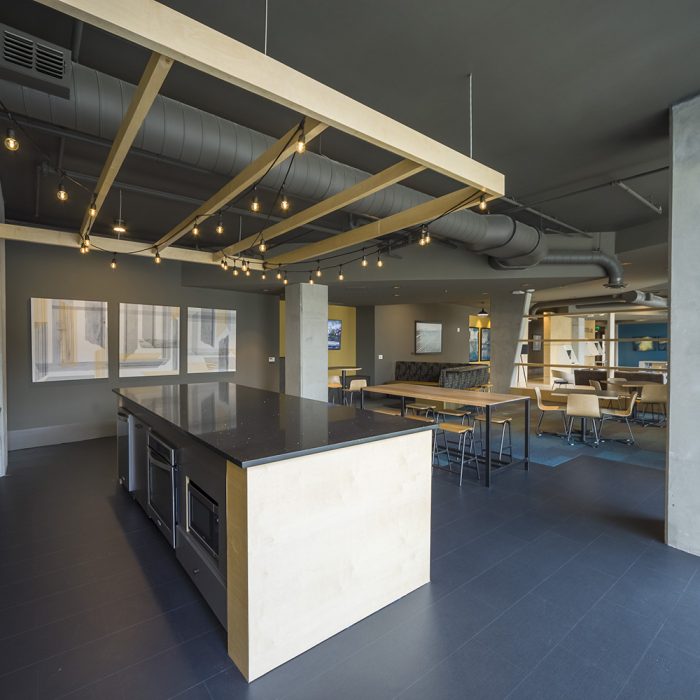 Modern lounging area with kitchen, tables, and chairs for residents