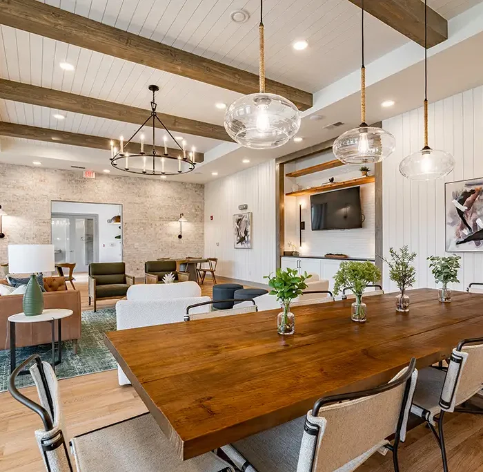 view of a large lounge in an apartment community with a big wood table, chandeliers, and wood beams