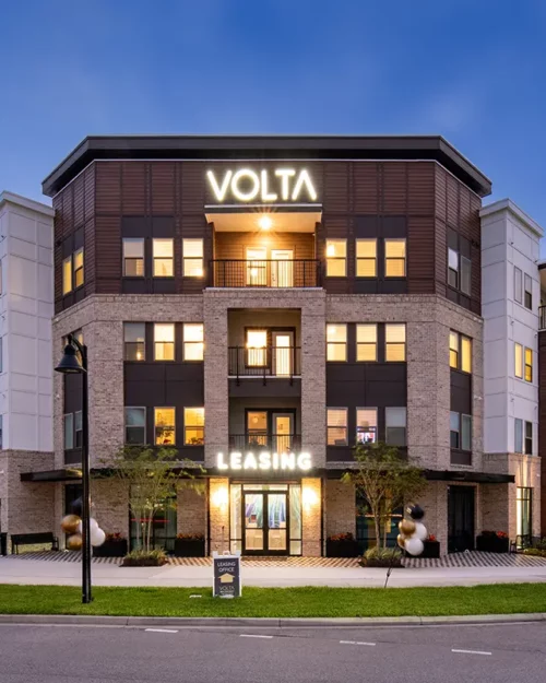 4 story apartment building in the evening with lighted signs that says "Volta"