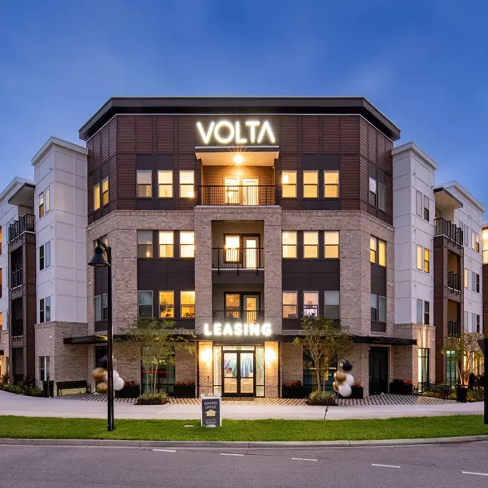 4 story apartment building in the evening with lighted signs that says "Volta"