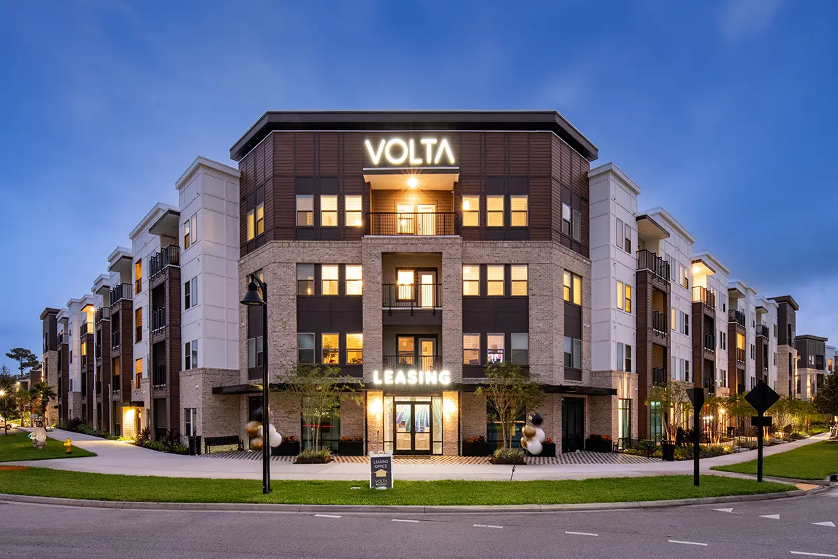 4 story apartment building in the evening with lighted signs that says "Volta"