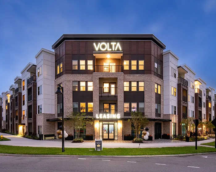 4 story apartment building in the evening with lighted signs that says "Volta"