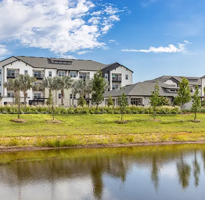 view of a lake with a 3 story apartment building and smaller 1 story building