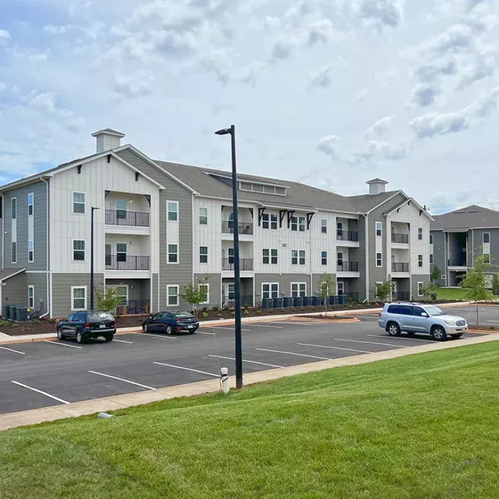 3 story apartment building with lawn and surface parking