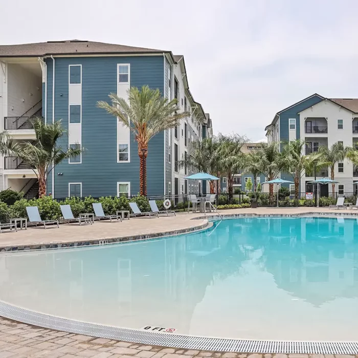 4 story apartment building with pool in the foreground and palm trees