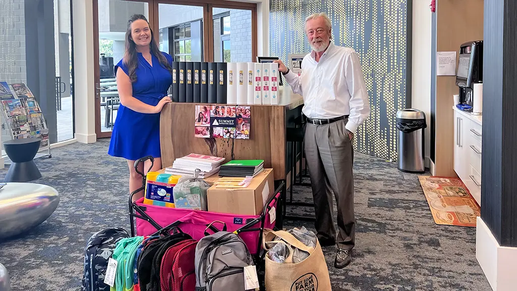 2 people standing in front of a large stack of school supplies