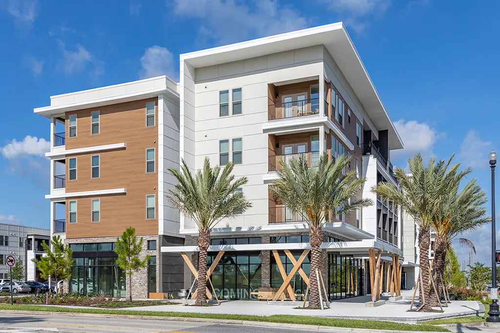 4 story apartment buildings with brown wood siding and white trim, with palm trees and blue sky