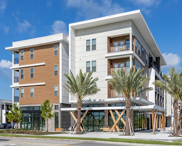 4 story apartment buildings with brown wood siding and white trim, with palm trees and blue sky