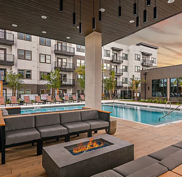 outdoor lounge with fire pit next to swimming pool and 4-story apartment building