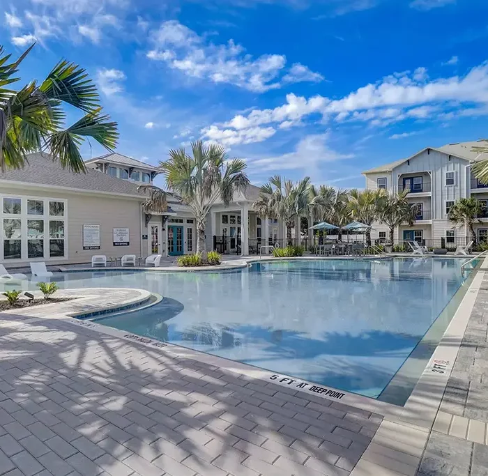 swimming pool and clubhouse building surrounded by palm trees, with an apartment building in the background