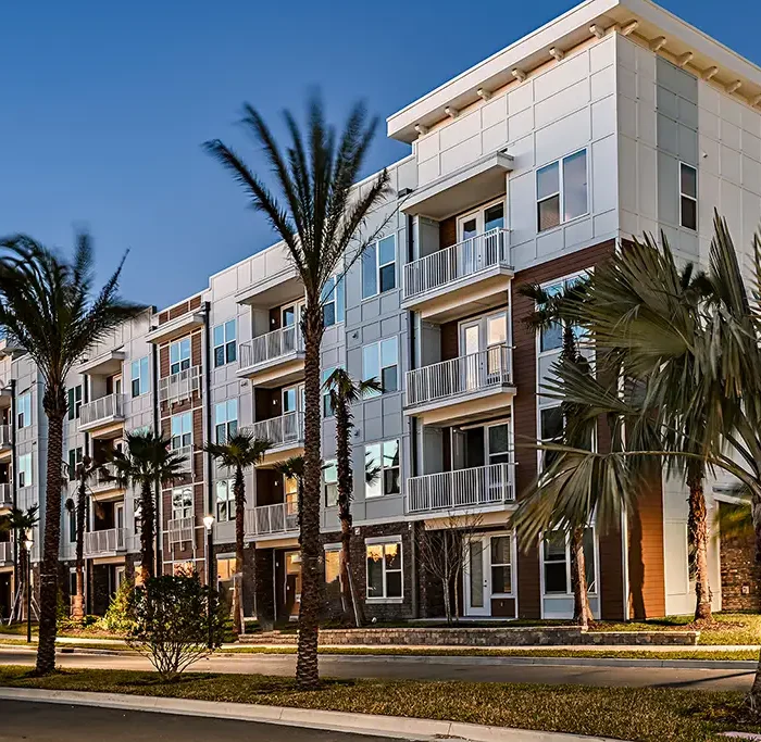 4 story apartment building with a flat roof and palm trees in front