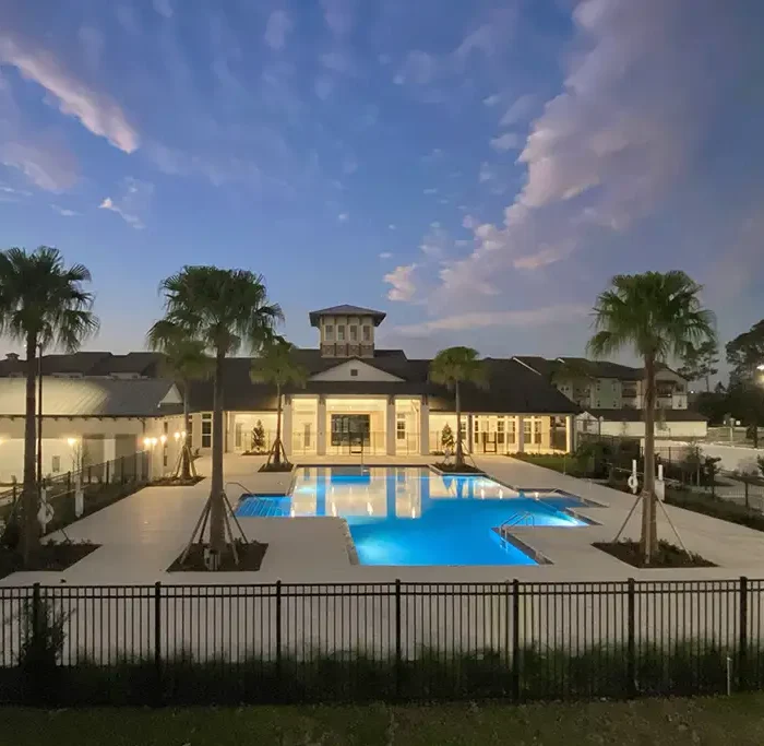 evening twilight photo of swimming pool and clubhouse with palm trees and buildings in the background