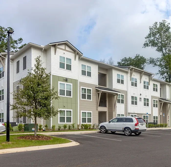 3 story apartment building in a parking lot surrounded by trees